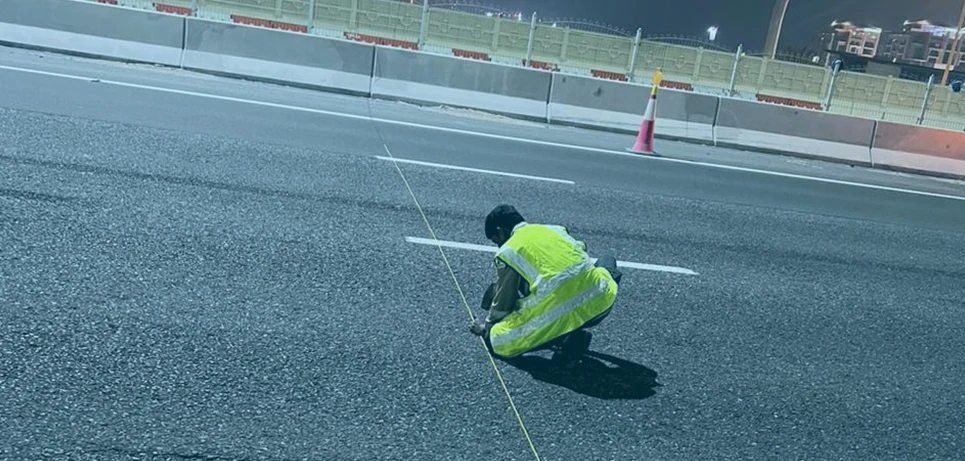 Survey engineering worker verifying reference string metrics across asphalt tracking plane pathways